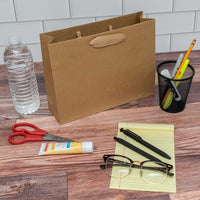 10.5x3x8.25 medium brown paper bag with ribbon handles on a desk with office supplies, water bottle, and glasses.